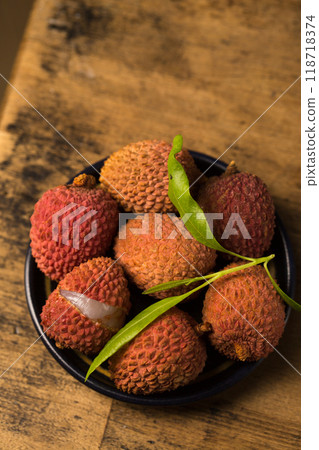 Small ripe tropical lychee berries on a black plate on a wooden background 118718374