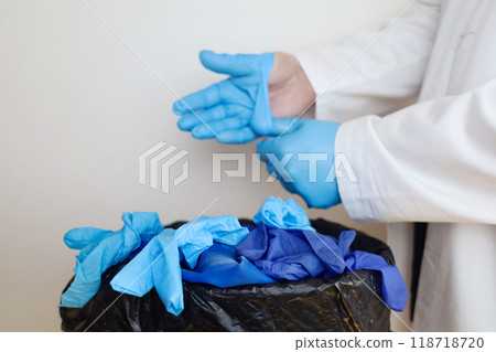 Doctor throws disposable gloves into trash bin. Medical waste disposal and treatment. Close up of medical worker's hands after work in hospital. 118718720