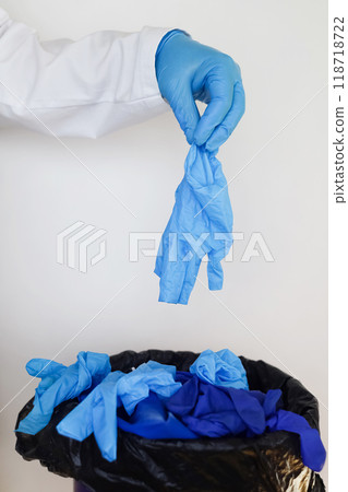 Doctor throws disposable gloves into trash bin. Medical waste disposal and treatment. Close up of medical worker's hands after work in hospital. 118718722