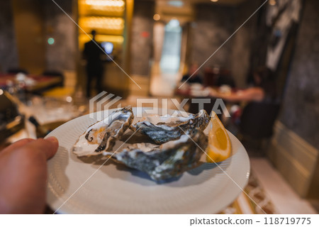 A lavish hotel dining area featuring a plate of fresh oysters with lemon, plush seating, ornate decor, and warm ambient lighting, highlighting luxury and sophistication. 118719775