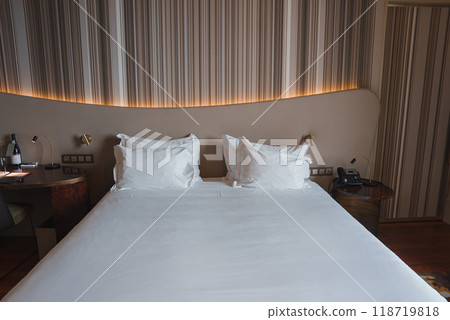 A beautifully designed hotel room featuring a large bed with crisp white linens, unique headboard with ambient lighting, and bedside tables with wine and telephone. A beautifully designed hotel room featuring a large bed with crisp white linens, unique headboard with ambient lighting, and bedside tables with wine and telephone. 118719818