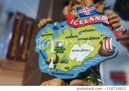 Detailed map of Iceland highlighting Akureyri, Myvatn, Gullfoss, and more, held by a figurine. Features puffin, Viking ship, geyser, and Icelandic flag. Detailed map of Iceland highlighting Akureyri, Myvatn, Gullfoss, and more, held by a figurine. Features puffin, Viking ship, geyser, and Icelandic flag. 118719822