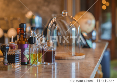 A sophisticated bar counter featuring a marble top, various bottles of oils and bitters, and a glass cloche. The ambient lighting and decor suggest a high-end luxury hotel. A sophisticated bar counter featuring a marble top, various bottles of oils and bitters, and a glass cloche. The ambient lighting and decor suggest a high-end luxury hotel. 118719827