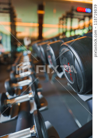 A row of dumbbells in a well-lit gym within a luxury hotel. The gym features large mirrors and ambient lighting, emphasizing both functionality and aesthetics. A row of dumbbells in a well-lit gym within a luxury hotel. The gym features large mirrors and ambient lighting, emphasizing both functionality and aesthetics. 118719839