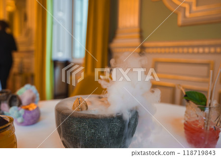 Elegant interior of a high-end hotel dining room with large windows and yellow curtains. A unique dish in a stone bowl emits vapor, showcasing artistic culinary style. 118719843
