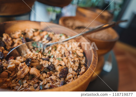 A detailed view of a wooden bowl filled with granola, nuts, seeds, and dried fruits, set in a luxury hotel dining area. Elegant presentation with rustic charm. 118719877