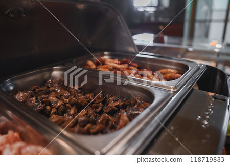 Close-up of a luxury hotel's buffet featuring sauteed mushrooms and assorted sausages in stainless steel chafing dishes. Sophisticated interior with ambient lighting. Close-up of a luxury hotel's buffet featuring sauteed mushrooms and assorted sausages in stainless steel chafing dishes. Sophisticated interior with ambient lighting. 118719883