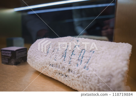 Neatly rolled towel with Vila Foz embroidery on wooden surface, next to elegant toiletries box. Reflective background adds depth, highlighting luxury ambiance. Neatly rolled towel with Vila Foz embroidery on wooden surface, next to elegant toiletries box. Reflective background adds depth, highlighting luxury ambiance. 118719884