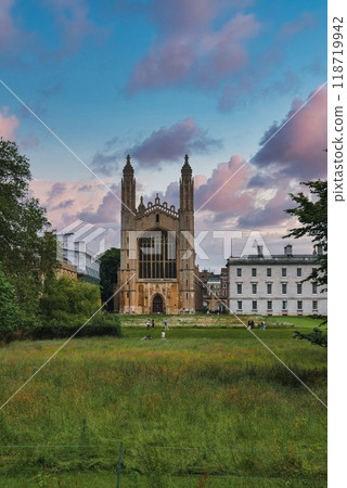 The iconic King's College Chapel in Cambridge, UK, with its Gothic architecture, lush green lawn, and a vibrant, partly cloudy sky in the background. 118719942