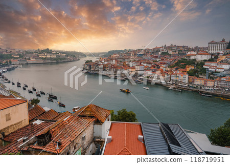 A breathtaking view of the Douro River in Porto, Portugal, featuring iconic red-tiled rooftops, historic buildings, and traditional Rabelo boats at sunset. 118719951