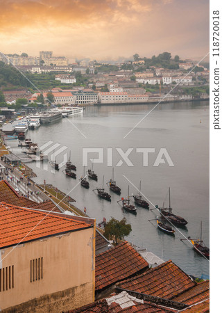 A picturesque scene of the Douro River in Porto, Portugal, featuring traditional Rabelo boats, terracotta rooftops, historic buildings, and a golden sky at sunrise. A picturesque scene of the Douro River in Porto, Portugal, featuring traditional Rabelo boats, terracotta rooftops, historic buildings, and a golden sky at sunrise. 118720018