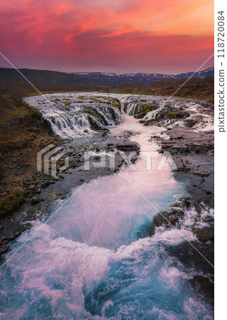 Stunning view of Bruarfoss waterfall in Iceland, featuring vibrant blue waters, rugged terrain, and a dramatic sunset sky with distant snow-capped mountains. Stunning view of Bruarfoss waterfall in Iceland, featuring vibrant blue waters, rugged terrain, and a dramatic sunset sky with distant snow-capped mountains. 118720084