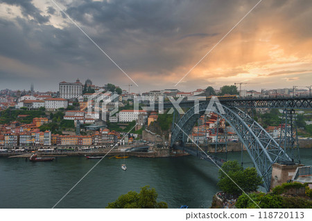 Iconic Dom Luis I Bridge spans the Douro River in Porto, Portugal, connecting the city's banks. Ribeira district's colorful buildings and dramatic sky enhance the scene. Iconic Dom Luis I Bridge spans the Douro River in Porto, Portugal, connecting the city's banks. Ribeira district's colorful buildings and dramatic sky enhance the scene. 118720113