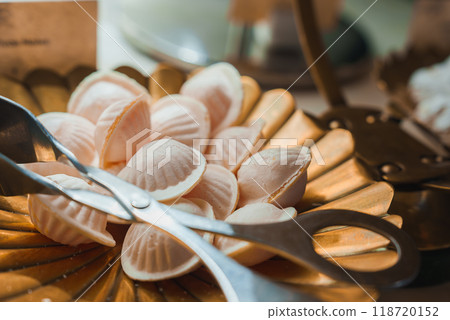 Close-up of a golden tray filled with delicate, shell-shaped confections in a high-end hotel or restaurant. Silver tongs are placed on the tray, ready for use. 118720152