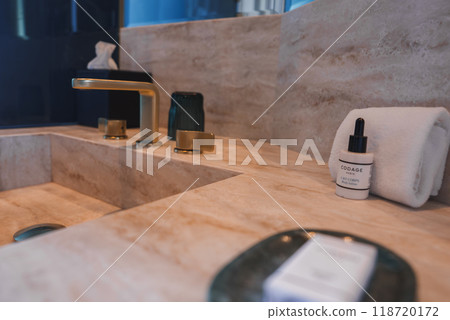 Elegant bathroom sink area featuring a light-colored marble countertop, gold faucet, and high-end amenities, suggesting a luxury hotel interior. Elegant bathroom sink area featuring a light-colored marble countertop, gold faucet, and high-end amenities, suggesting a luxury hotel interior. 118720172