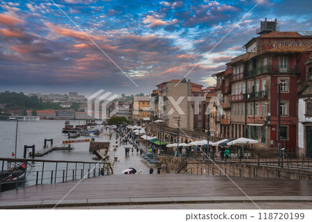 Bustling riverside promenade with colorful historic buildings, outdoor cafes, and traditional Rabelo boats on the Douro River in Porto, Portugal. Bustling riverside promenade with colorful historic buildings, outdoor cafes, and traditional Rabelo boats on the Douro River in Porto, Portugal. 118720199