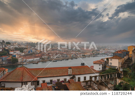 Stunning view of Porto, Portugal at sunset with the Douro River dividing the city. Traditional red-tiled roofs and a mix of historic and modern architecture are visible. Stunning view of Porto, Portugal at sunset with the Douro River dividing the city. Traditional red-tiled roofs and a mix of historic and modern architecture are visible. 118720244
