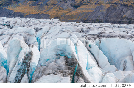 Stunning aerial view of a glacier in Iceland, showcasing deep crevasses and beautiful blue ice. The light reflects off the icy surface, highlighting its natural beauty. 118720279