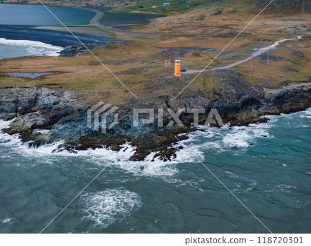 A stunning aerial view of Iceland's rocky coastline featuring a small orange building on a cliff, deep blue ocean waters, and white waves crashing against the rocks. A stunning aerial view of Iceland's rocky coastline featuring a small orange building on a cliff, deep blue ocean waters, and white waves crashing against the rocks. 118720301
