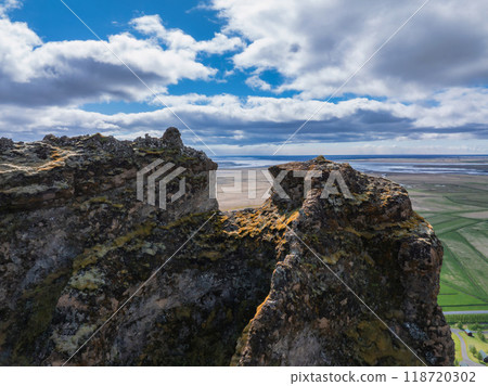 Dramatic aerial view of two rocky cliffs with a gap revealing a flat, green landscape in Iceland. Blue sky with white clouds enhances the rugged beauty. Dramatic aerial view of two rocky cliffs with a gap revealing a flat, green landscape in Iceland. Blue sky with white clouds enhances the rugged beauty. 118720302