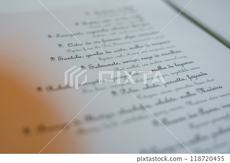 Detailed view of a luxury hotel's menu featuring artistic cursive text in Portuguese. The soft lighting and blurred background enhance the upscale ambiance. Detailed view of a luxury hotel's menu featuring artistic cursive text in Portuguese. The soft lighting and blurred background enhance the upscale ambiance. 118720455