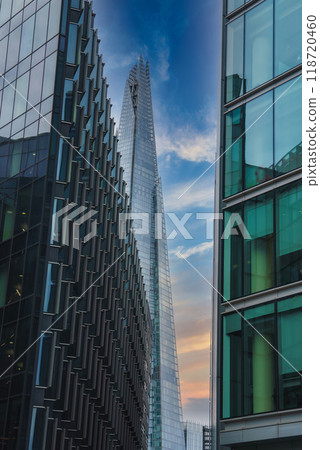 The Shard stands tall against a partly cloudy sky during sunset in London, UK. Flanked by modern glass buildings, the low angle emphasizes its grandeur. 118720460