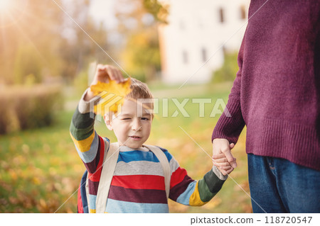 Mother takes her child to educational institution and walking in public autumnal park. 118720547