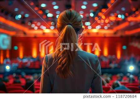 An individual looks toward the stage in a brightly lit auditorium, as attendees gather for a business conference focused on networking and learning An individual looks toward the stage in a brightly lit auditorium, as attendees gather for a business conference focused on networking and learning 118720684