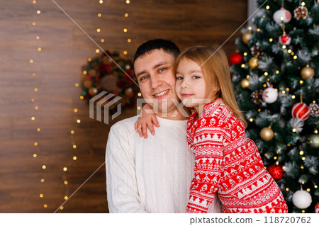 A young dad holds his 6-year daughter while standing by the Christmas tree. A young dad holds his 6-year daughter while standing by the Christmas tree. 118720762
