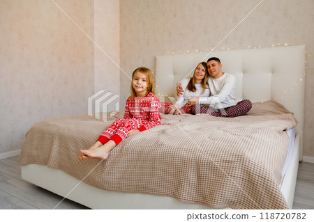A boy and a girl are lying between their parents on the bed, reading a book in the Christmas spirit. 118720782