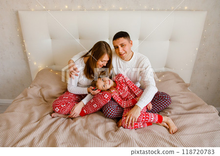 Young parents are hugging their beloved daughter on the bed in the bedroom Young parents are hugging their beloved daughter on the bed in the bedroom 118720783