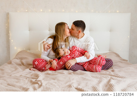 Young parents are hugging their beloved daughter on the bed in the bedroom Young parents are hugging their beloved daughter on the bed in the bedroom 118720784