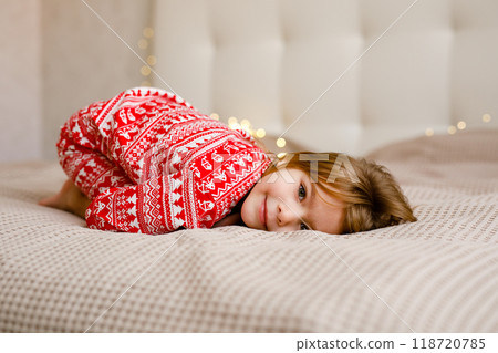 A girl in a Christmas pajama is lying on the bed and smiling A girl in a Christmas pajama is lying on the bed and smiling 118720785