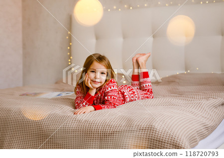 A girl in a Christmas pajama is lying on the bed and smiling A girl in a Christmas pajama is lying on the bed and smiling 118720793