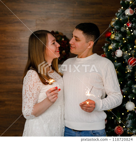A romantic pair is hugging and holding Bengal lights in front of a Christmas tree 118720824