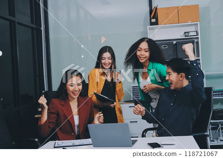 Young corporate employees sitting in office looking at laptop screen reading good news excited happy team diverse people celebrating victory win command success excellent result professional teamwork 118721067