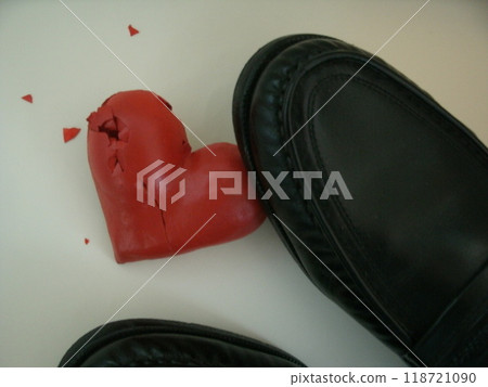 A broken red heart lying on the floor and a black leather shoe stepping on it A broken red heart lying on the floor and a black leather shoe stepping on it 118721090