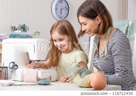 Little girl trying to make dress for her doll with her teacher 118722450
