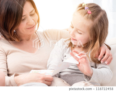 Happy smiling mom looking at the mother's day greeting card made by daughter sitting on sofa with little child 118722458