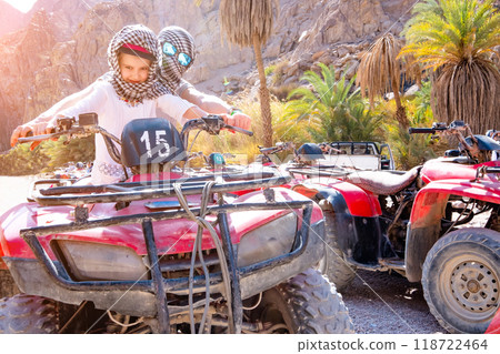 A pair, kid with trainer are riding on red quad bike in desert safari 118722464