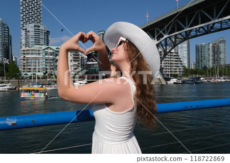 Slender young girl in white hat and dress stands on pier in Vancouver looking at ship and sails Beautiful woman on a ship at sunset.  118722869