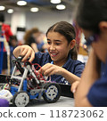 A young girl participating in robotic competition, as she adjusts her robot. Her focused hands skillfully assemble parts, surrounded by peers, embodying innovation in tech. 118723062