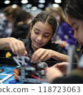A young girl participating in robotic competition, as she adjusts her robot. Her focused hands skillfully assemble parts, surrounded by peers, embodying innovation in tech. 118723063