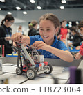 A young girl participating in robotic competition, as she adjusts her robot. Her focused hands skillfully assemble parts, surrounded by peers, embodying innovation in tech. 118723064
