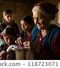 An elderly woman proudly teaches young girls traditional embroidery. Her weathered hands guide young girls, passing on cultural heritage in a simple village setting filled with warmth. 118723071