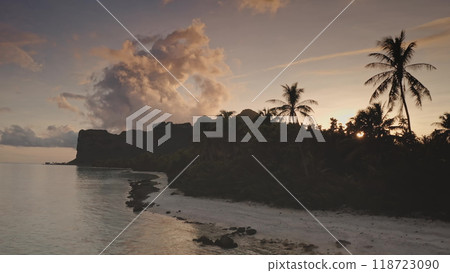 Drone flight over tropical island beach, palm trees silhouette against golden sunset light, dramatic volcanic peaks of Maupiti archipelago in French Polynesia. Beautiful landscape of untouched nature Drone flight over tropical island beach, palm trees silhouette against golden sunset light, dramatic volcanic peaks of Maupiti archipelago in French Polynesia. Beautiful landscape of untouched nature 118723090