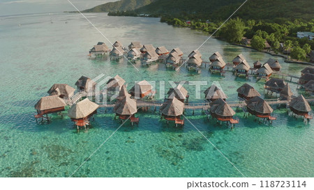 Luxurious overwater bungalows huts with thatched roofs standing in rows on turquoise lagoon water of Moorea island in French Polynesia. Exotic travel vacation getaway, romantic honeymoon. Aerial shot 118723114