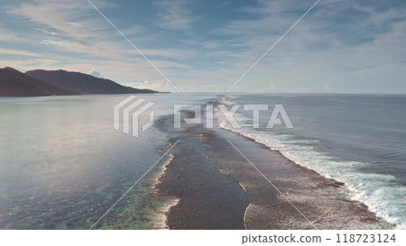 Aerial drone flight over shallow coral barrier reef tropical island coast with crystal clear water and waves breaking calm surface. Natural beauty relaxation landscape. Wild nature travel background Aerial drone flight over shallow coral barrier reef tropical island coast with crystal clear water and waves breaking calm surface. Natural beauty relaxation landscape. Wild nature travel background 118723124