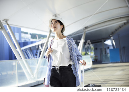 A full-body shot of a female traveler pulling a suitcase in an airport connecting corridor. 118723484