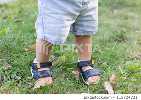 Babys feet in too small sandals walk on the green grass in a park Babys feet in too small sandals walk on the green grass in a park 118724721